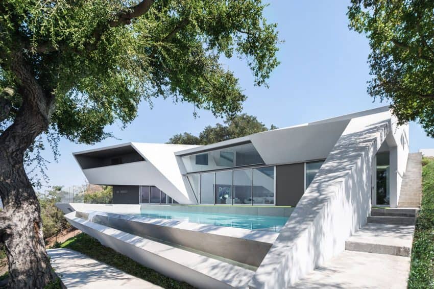 Futuristic modern house with sleek architectural design, large glass windows, and outdoor pool, surrounded by lush green trees, showcasing innovative contemporary architecture.