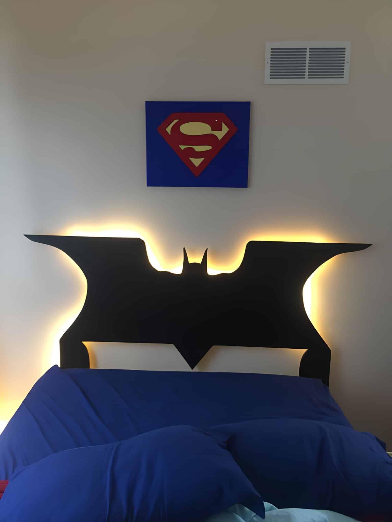 Black Batman-shaped headboard with backlit glow under Superman wall art