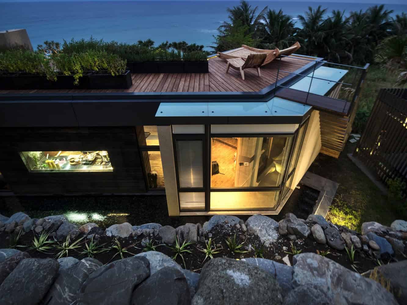 Modern contemporary house with glass walls, rooftop terrace, and ocean view, showcasing innovative architectural design and integration with natural surroundings.