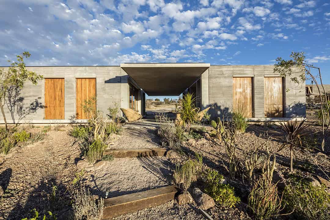 Modern desert home with concrete and wood accents, landscaped with drought-tolerant plants, under a bright blue sky.