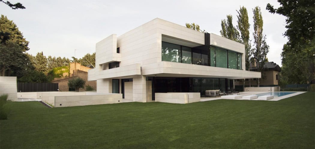 Contemporary modern house with sleek white exterior, large glass windows, and minimalist design in a lush green landscape.
