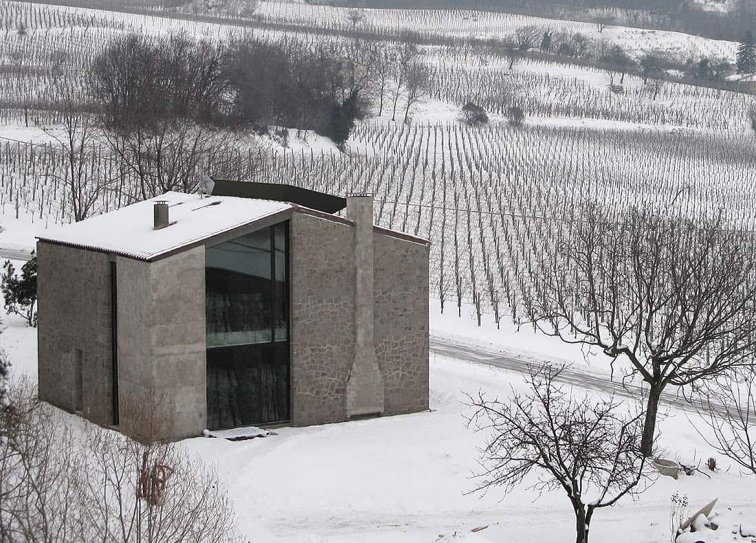 Contemporary modern house with stone facade in a snow-covered landscape surrounded by vineyards and leafless trees.