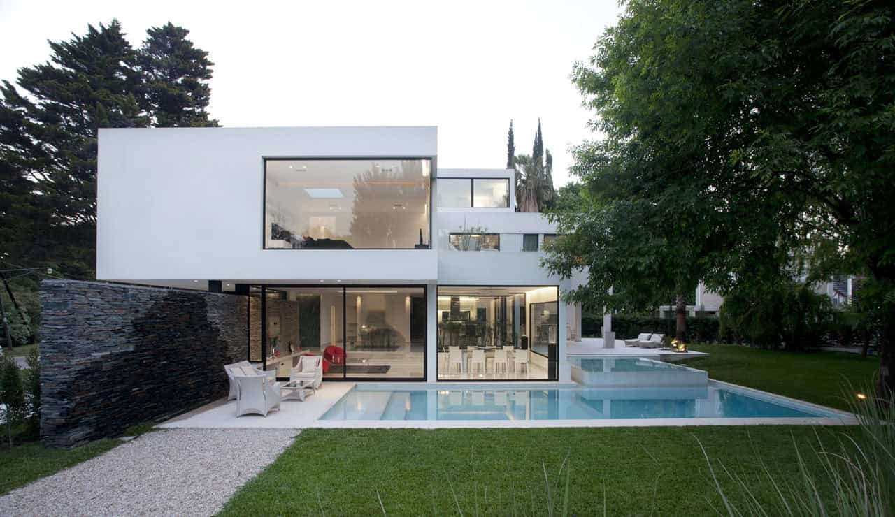 Modern minimalist white house with large glass windows, outdoor pool, and landscaped garden, showcasing contemporary architecture and innovative design.