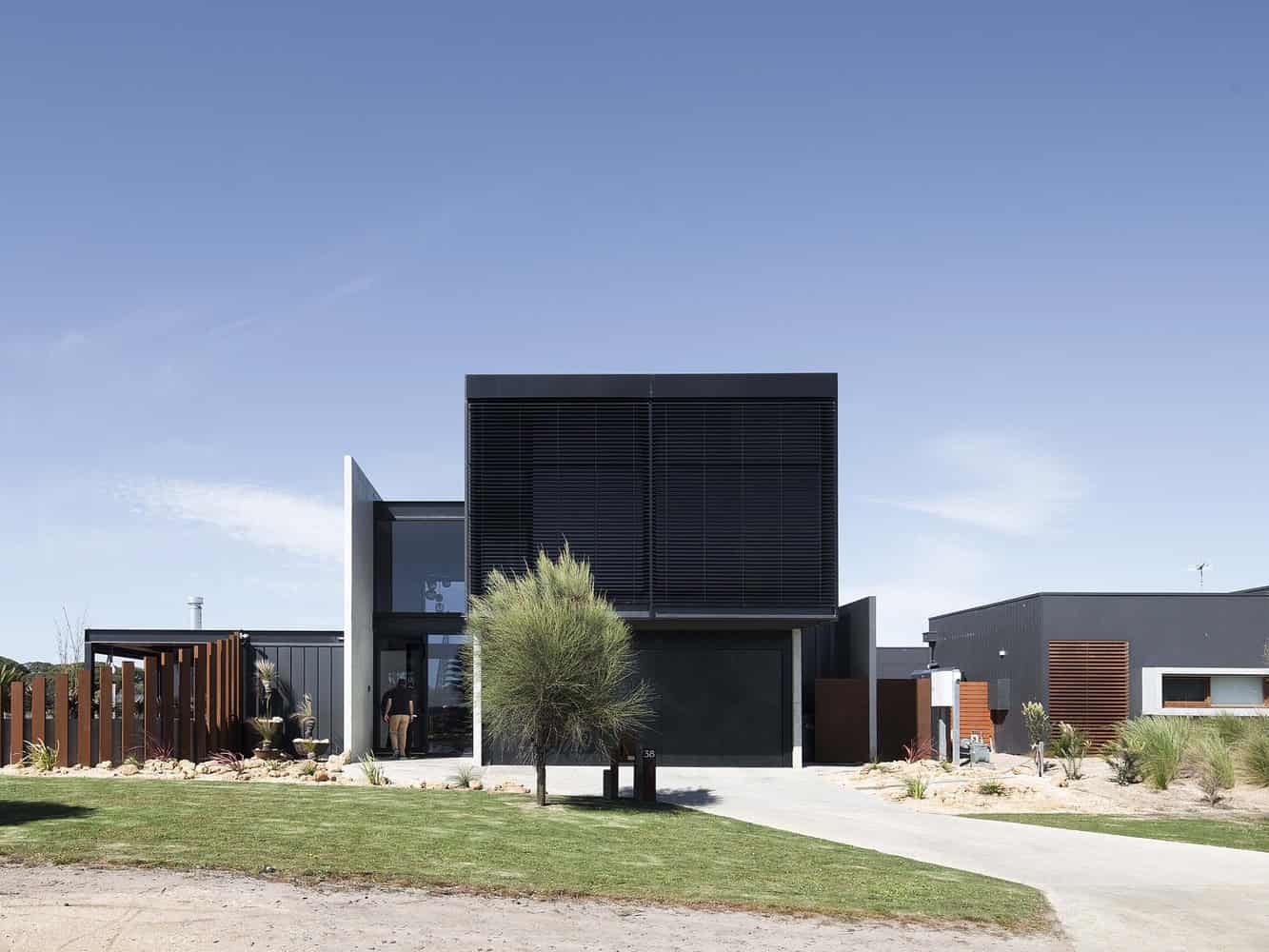 Modern black and gray minimalist residential house with clean lines, contemporary architecture, and outdoor landscape design featuring desert plants and a well-maintained lawn.
