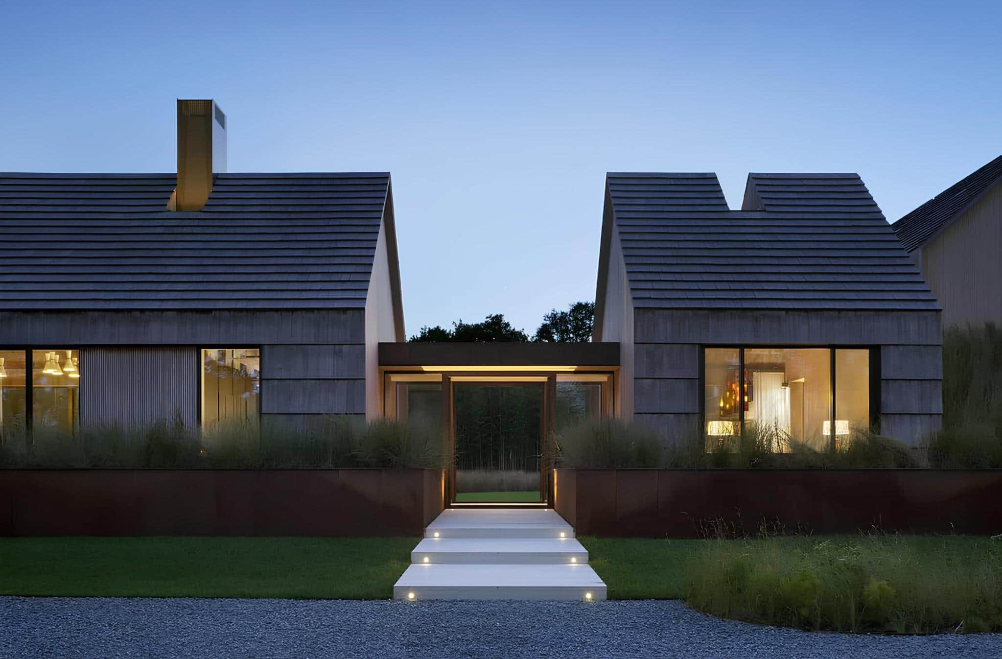 Contemporary modern house with sleek wooden exterior and large glass windows showcasing stylish interior lighting at dusk.