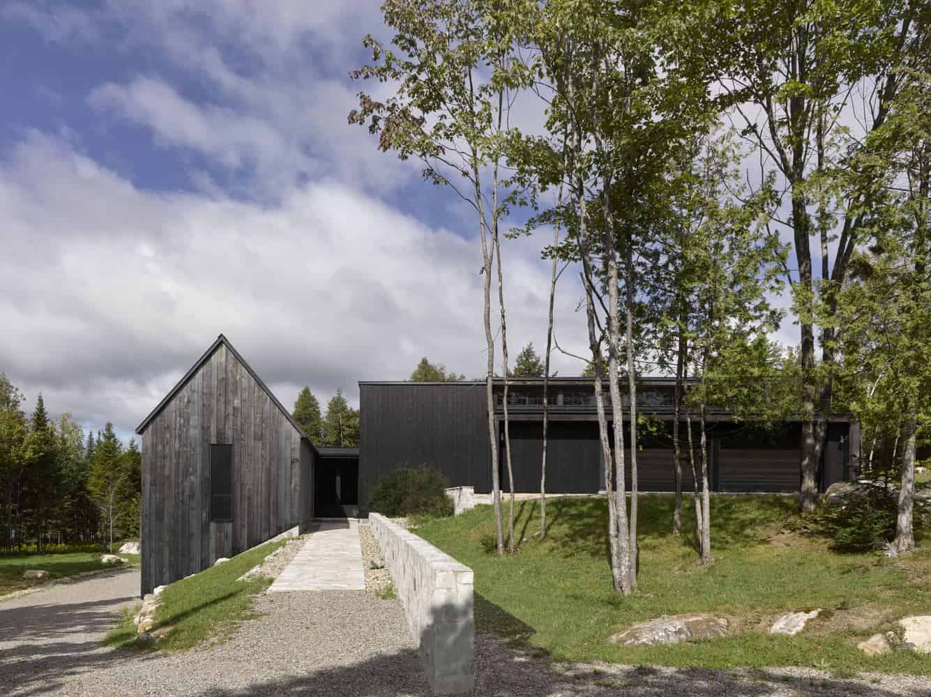 Modern black and gray minimalist house with wooden accents set among trees, showcasing contemporary architecture and landscape design.