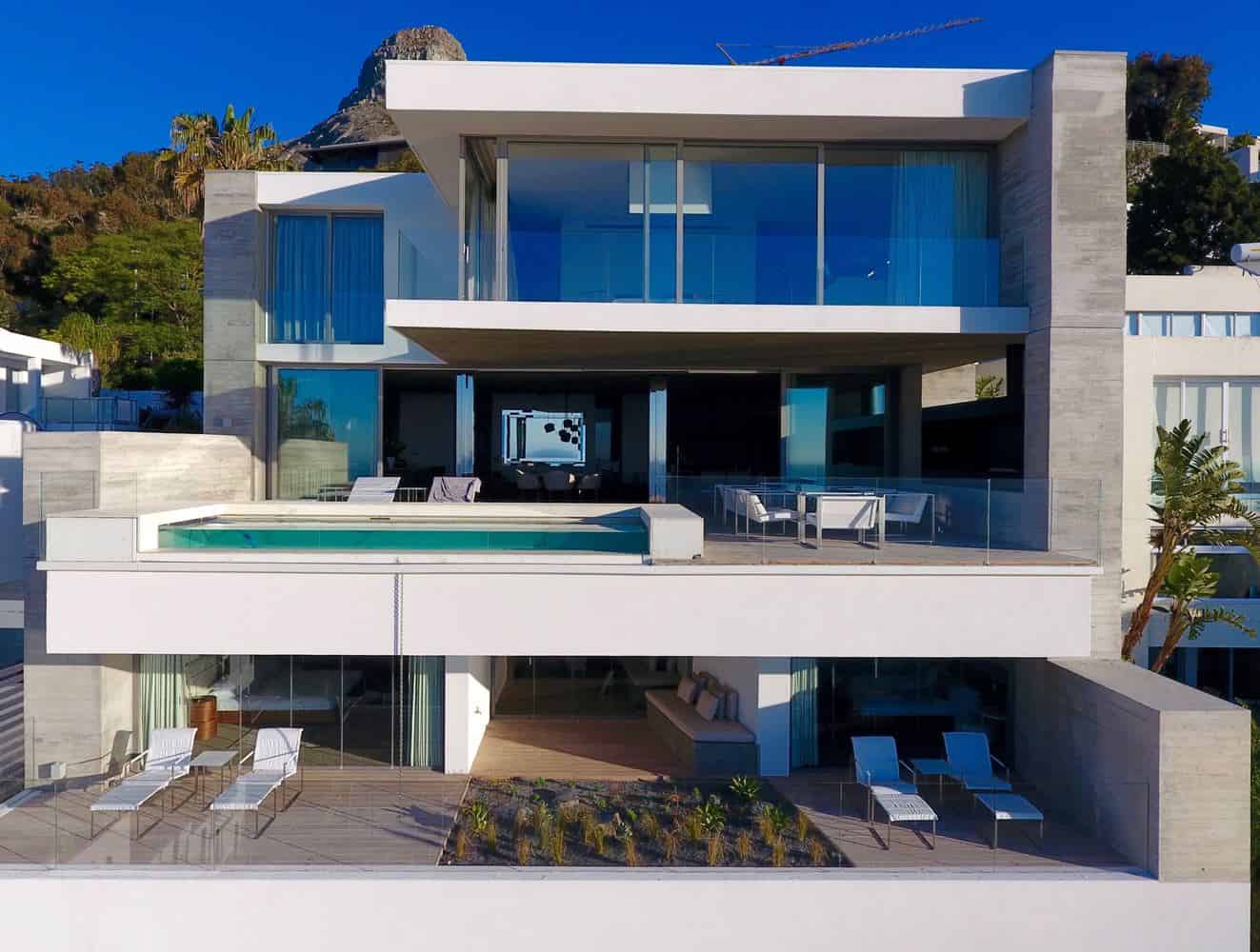 Modern luxury beachfront house with large glass windows and rooftop pool, featuring contemporary architectural design and outdoor lounge area.