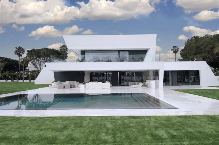 Modern luxury villa with contemporary architectural design and sleek white exterior. Features spacious outdoor patio, swimming pool, and lush green lawn. Perfect example of upscale residential architecture.
