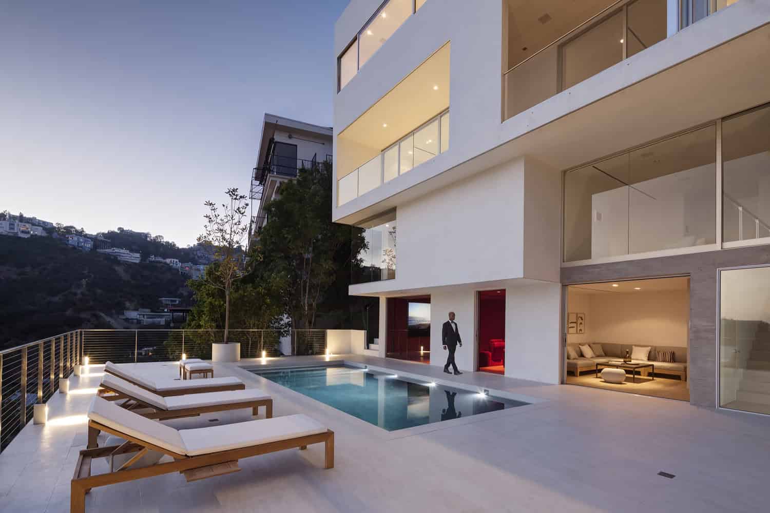 Contemporary modern house with an outdoor swimming pool, minimalist architecture, and panoramic city views at dusk. Elegant outdoor lounge area with sunbeds, outdoor lighting, and sleek design.