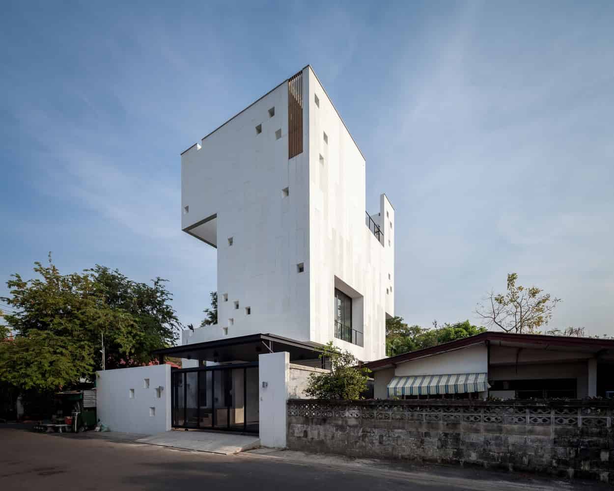 Contemporary minimalist white residential building with geometric design and unique window placements, showcasing modern architecture and innovative urban housing solutions on a quiet street.