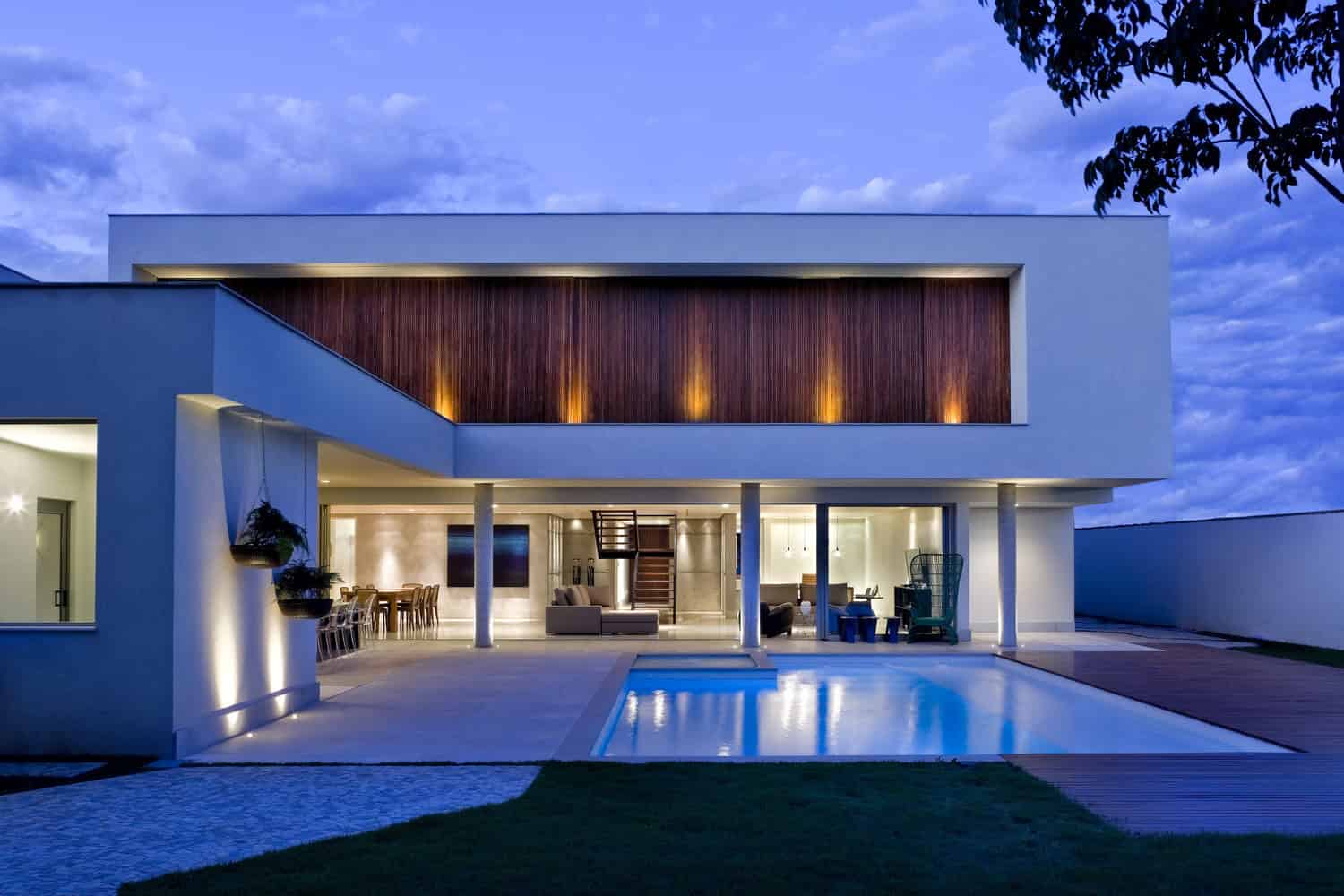 Contemporary modern house exterior with sleek minimalist architecture, illuminated by ambient lighting at dusk, featuring a swimming pool and open-plan outdoor living space.