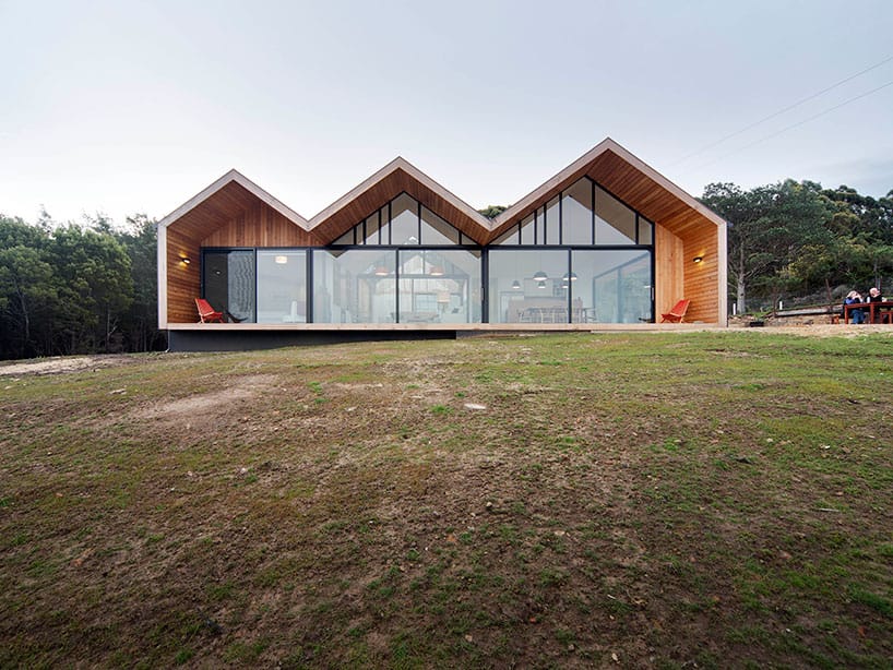 Modern architectural house with a distinctive zigzag roof design featuring large glass windows and wooden accents in a natural landscape setting.