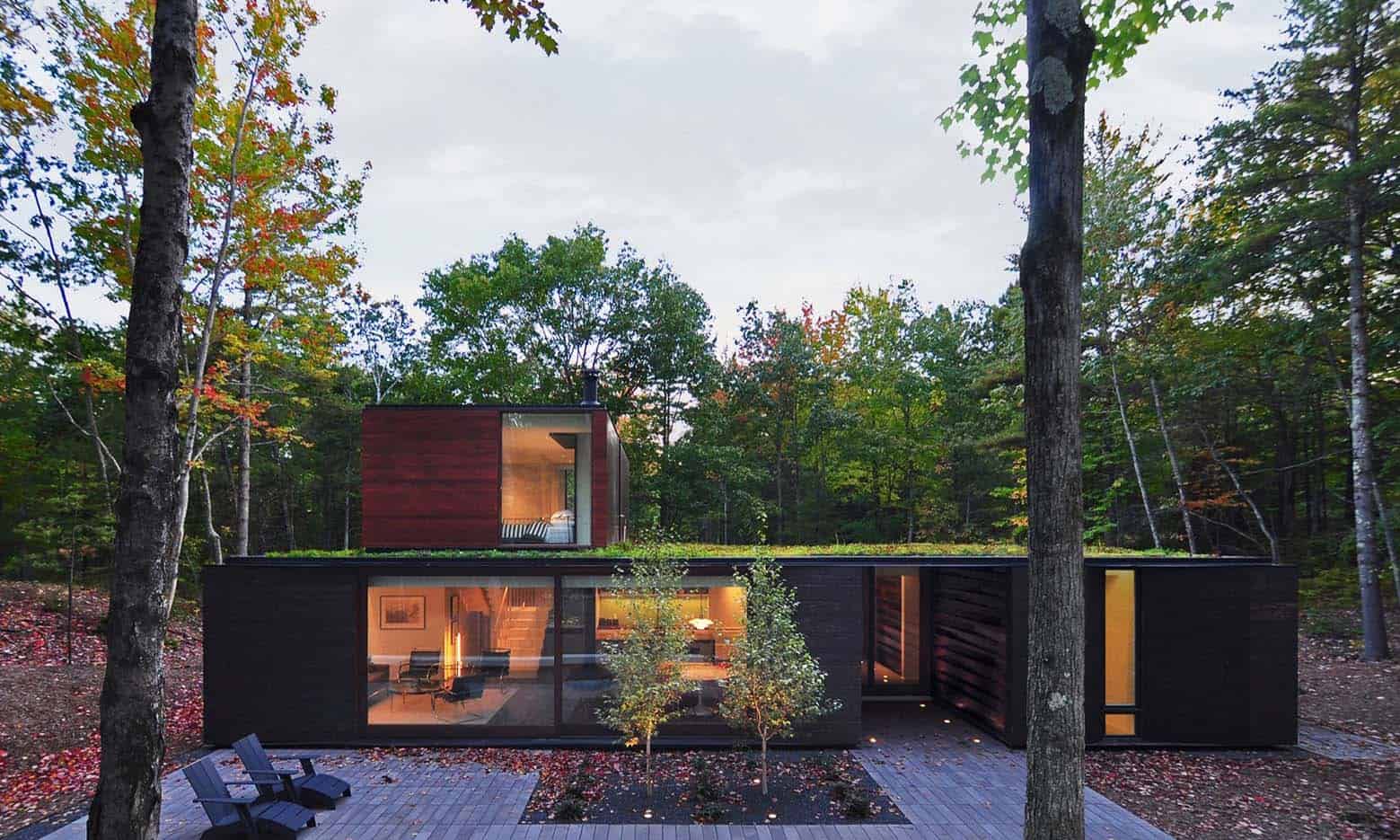 Contemporary modern house design with dark wooden exterior, large glass windows, and minimalist architecture integrated into a lush forest setting. Perfect for architecture art designs enthusiasts.