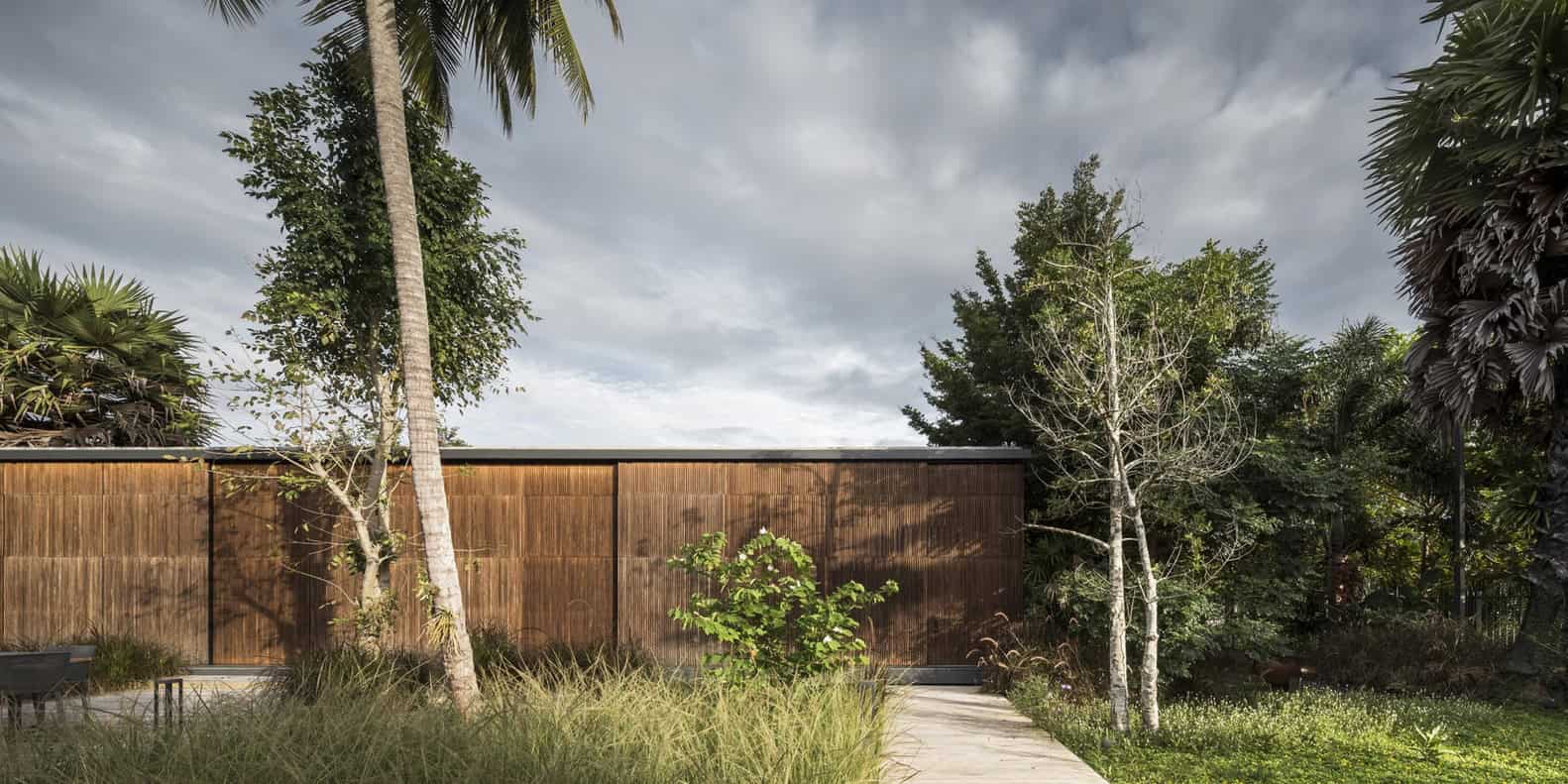 Contemporary tropical garden with wooden privacy fence, lush greenery, palm trees, and modern landscape design elements.