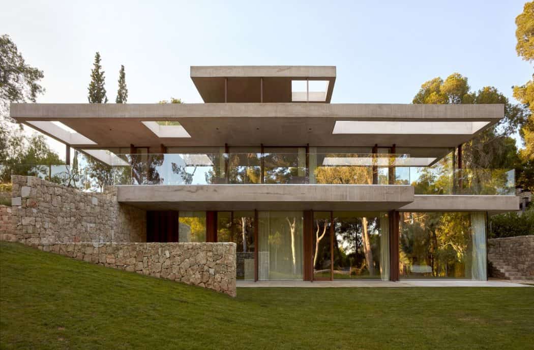 Sleek modern house with expansive glass windows and concrete balconies set in a lush green landscape.