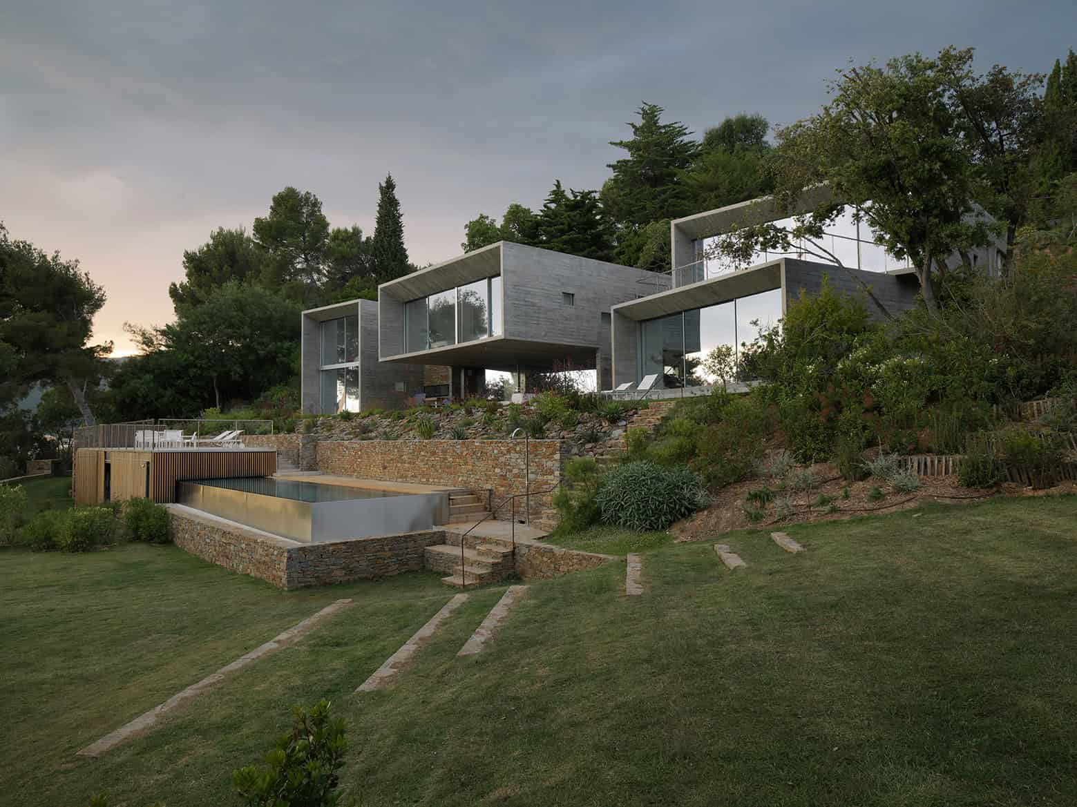 Contemporary modern house with large glass windows and unique geometric design on hillside with landscaped yard and outdoor pool.