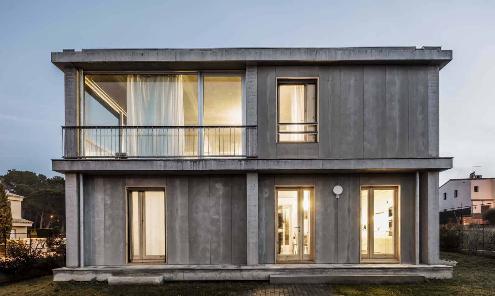 Sleek modern concrete house with large glass windows and a spacious balcony, showcasing contemporary architectural design and minimalist style.