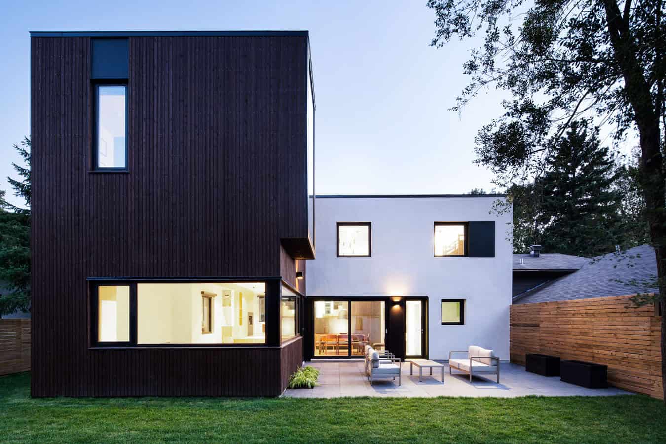 Contemporary modern house with minimalist design, black wooden and white stucco exterior, outdoor patio area, stylish furniture, surrounded by lush greenery and trees.