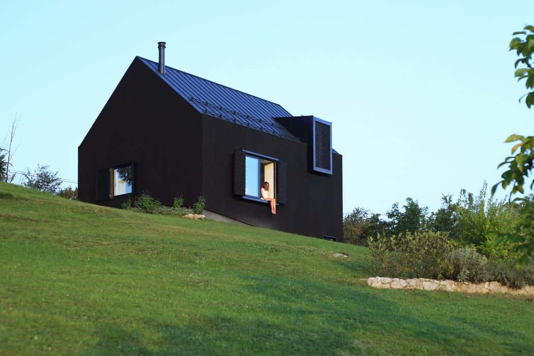 Modern black house with unique architectural design, large windows, and a sloped green lawn, highlighting contemporary architecture and innovative home design.