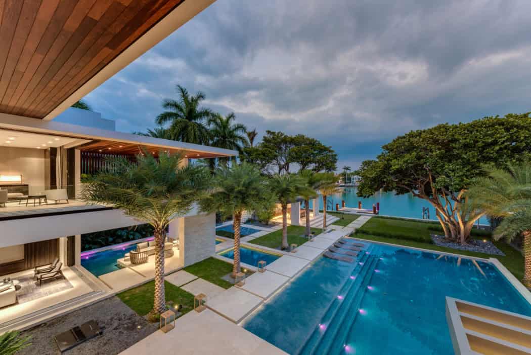 Luxurious modern waterfront house with infinity pool, tropical palm trees, and contemporary architecture, showcasing upscale residential design and outdoor living spaces.