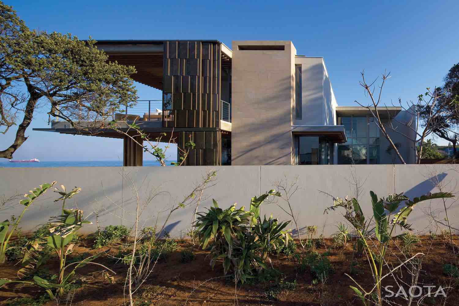 La Lucia by SAOTA & ARRCC — Beachfront façade with screening La Lucia house exterior on South Africa’s north coast with articulated bronze screens and coastal vegetation.