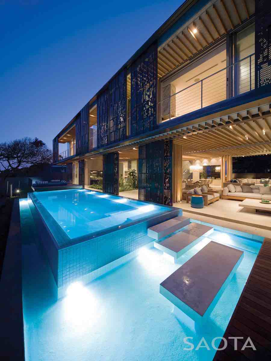 La Lucia — Evening ambience La Lucia residence at dusk with warm interior glow behind patterned bronze screens.