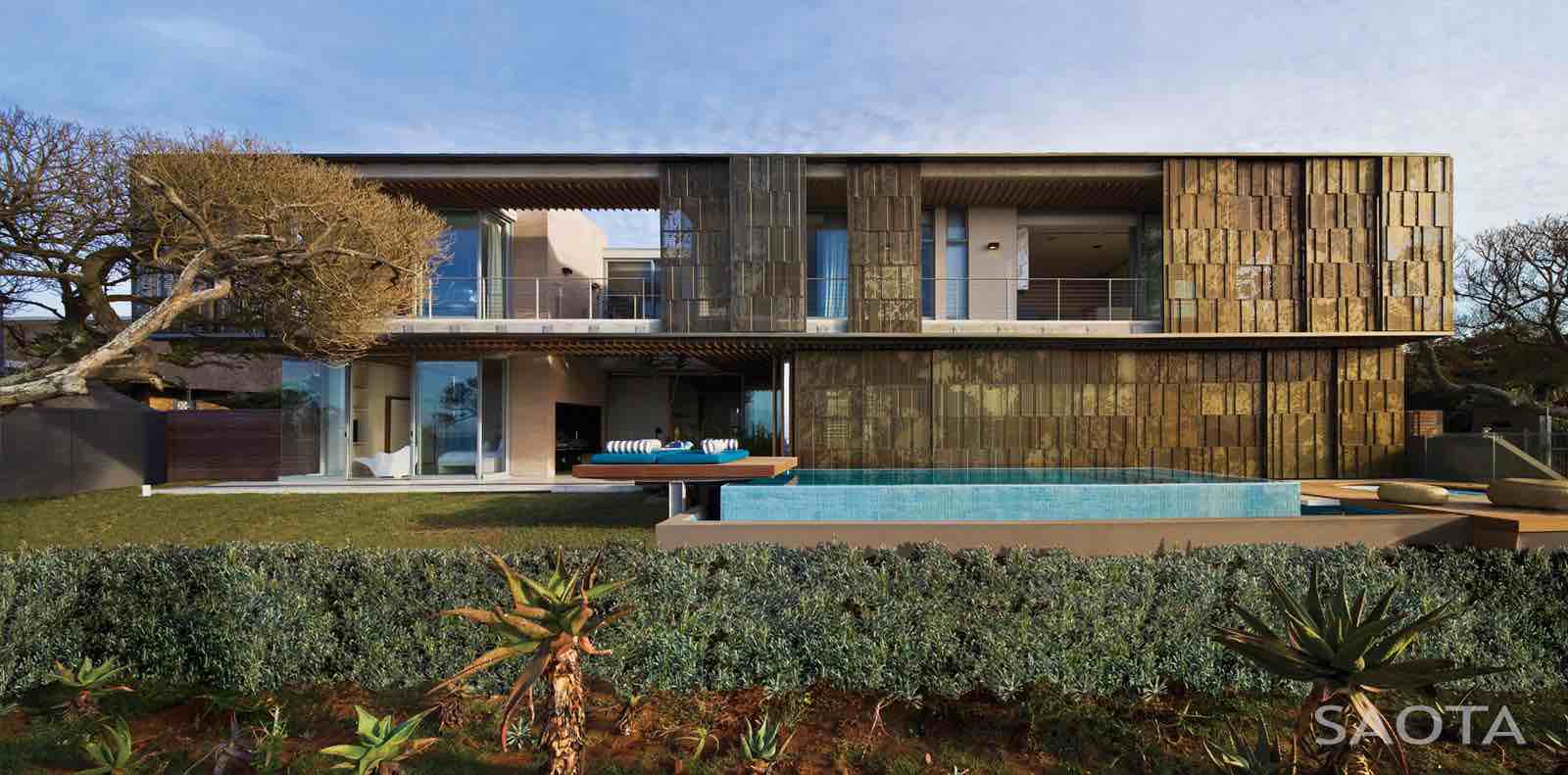 Contemporary modern house with mixed stone and glass exterior, flat roof, and outdoor pool, blending natural materials with sleek architectural design, set in landscaped garden.