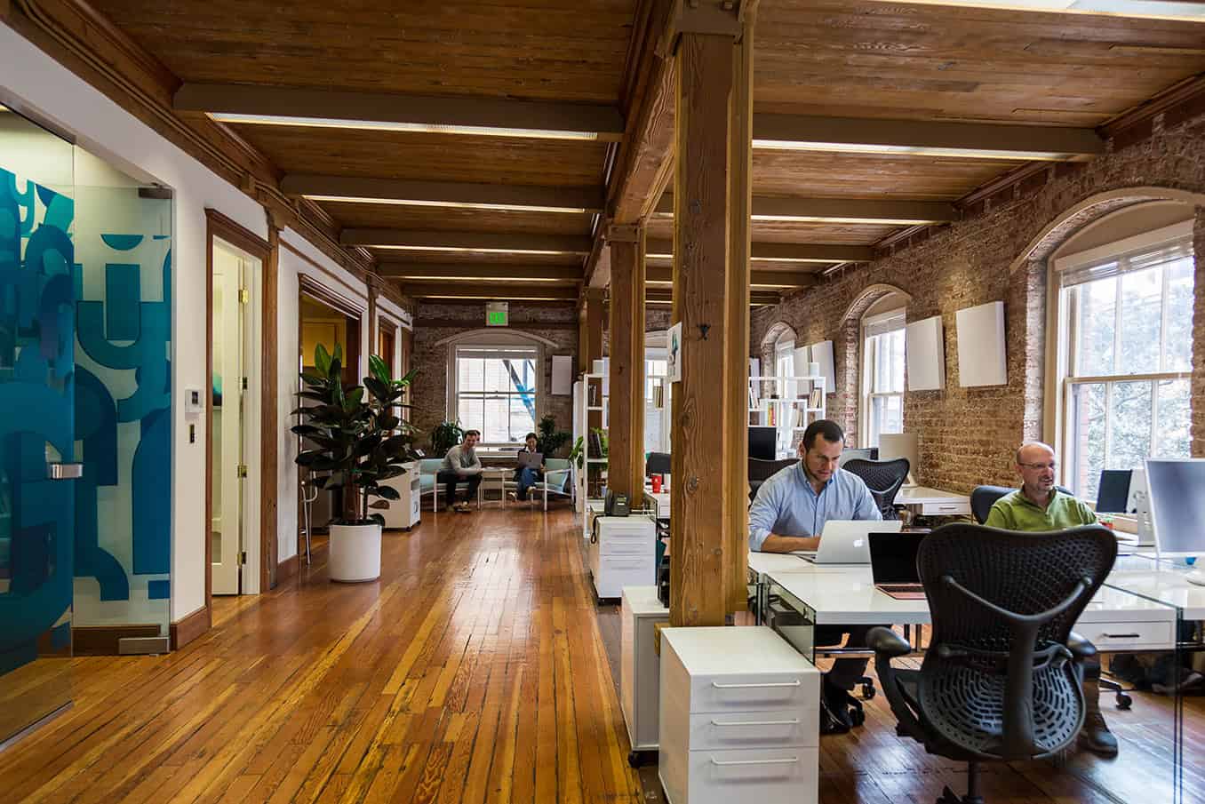 Modern office interior with exposed brick walls, wooden beams, and large windows, highlighting contemporary architectural design and stylish workspace decor.