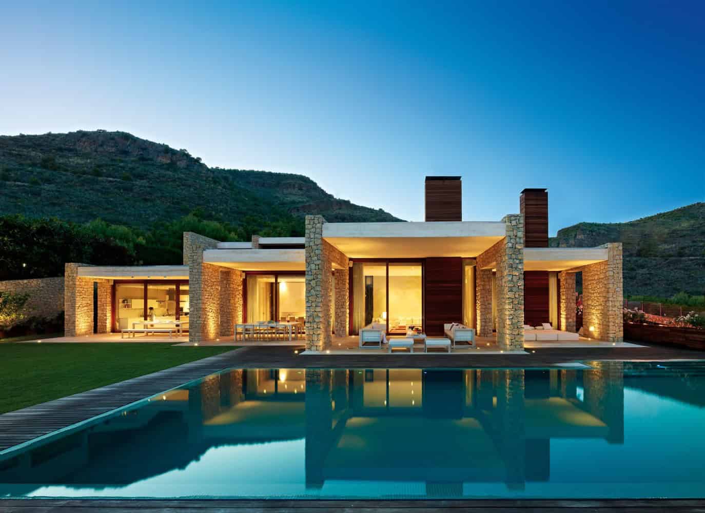 Contemporary modern house with stone and wood accents, large glass doors, outdoor pool, and mountain backdrop, showcasing luxury architecture and elegant outdoor design.