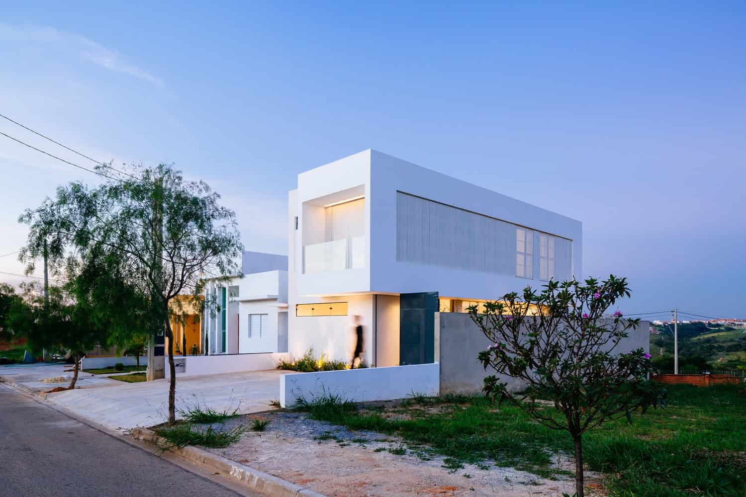 Modern minimalist white house with clean lines and large windows, contemporary architecture design, surrounded by greenery, at dusk.