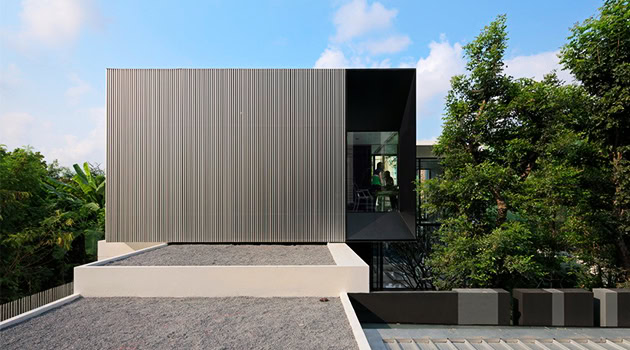 Sleek modern residential building with minimalist design, featuring metal cladding and large glass windows amidst lush greenery, exemplifying contemporary architecture and innovative design.