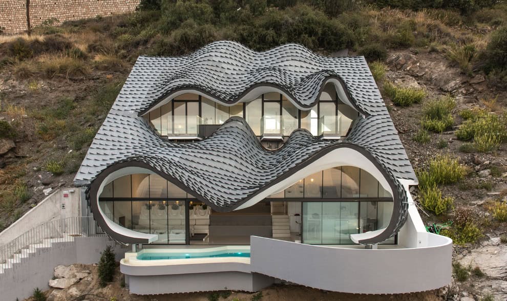 Unique modern house with wavy architectural roof design on a hillside, blending innovative architecture with natural surroundings.
