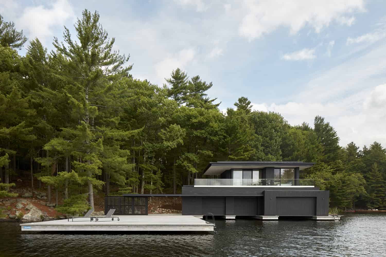 Modern lakeside house with sleek black exterior and large glass windows surrounded by lush green trees, showcasing contemporary architecture and luxury waterfront living.