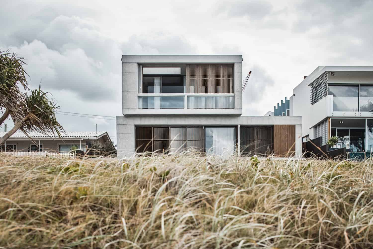 Modern minimalist concrete house with large glass windows and wooden accents, situated in a natural grassy landscape. Contemporary architecture with clean lines and innovative design.