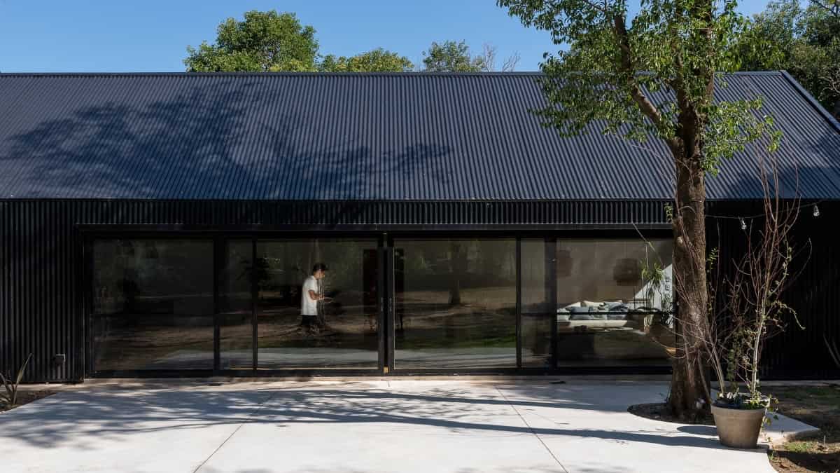 Modern black metal exterior house with large glass sliding doors, surrounded by greenery, showcasing contemporary architecture and minimalist design.