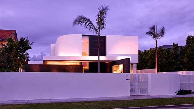 Modern luxury house with sleek geometric design and elegant white facade, surrounded by palm trees and a minimalist fence, showcasing innovative architecture and contemporary design elements.