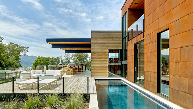 Sleek modern house with a spacious outdoor deck, swimming pool, and glass railing, showcasing contemporary architecture and outdoor living design.