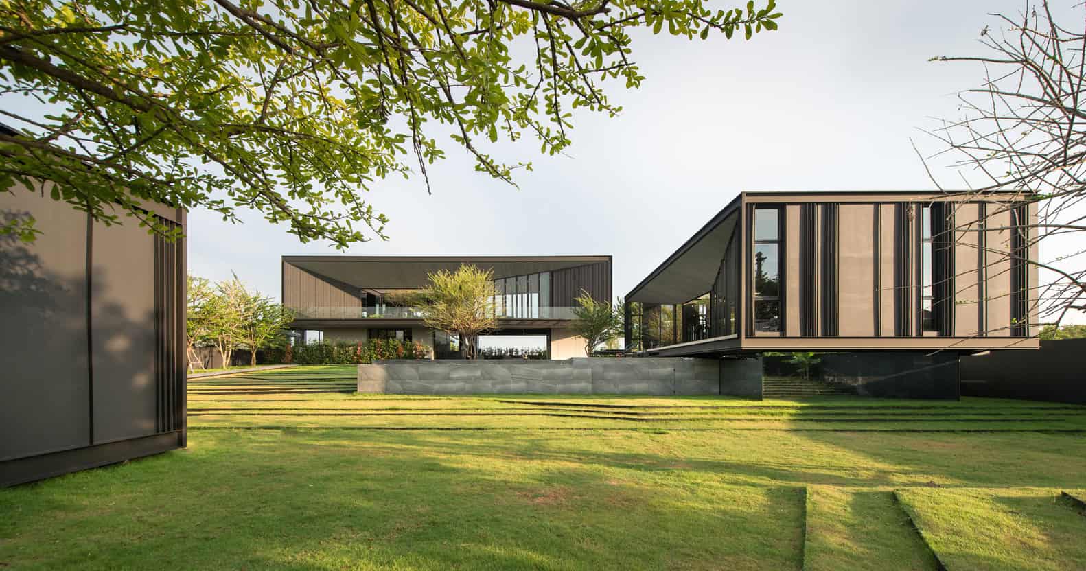 Modern luxury residential architecture with sleek black and beige exterior, expansive glass windows, and landscaped garden setting.