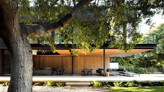 Stylish modern house with open-concept design, wooden accents, and outdoor seating area surrounded by lush greenery and trees.