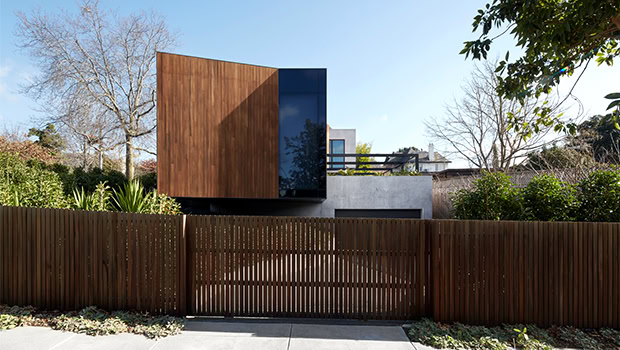 Sleek modern house with wooden and black facade, minimalist design, surrounded by lush greenery and wooden fence, showcasing contemporary architecture and innovative exterior styling.