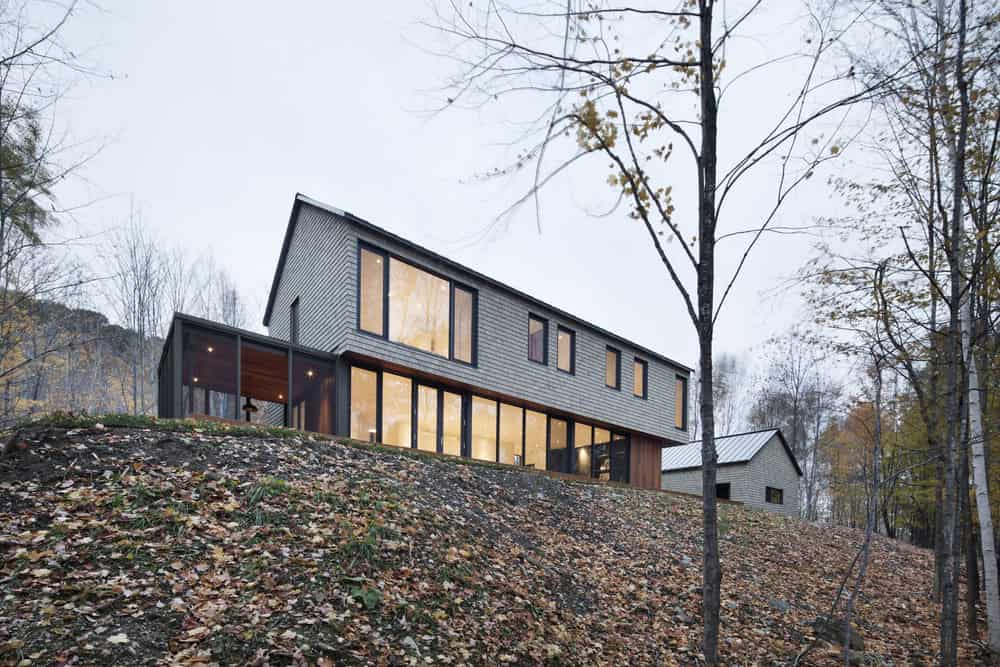 Contemporary modern house with large glass windows, situated on a wooded hillside surrounded by autumn trees, showcasing innovative architecture design.