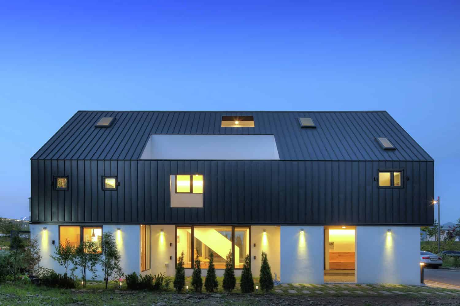 Modern black and white contemporary house with sleek metal roof, large windows, and outdoor lighting, showcasing innovative architectural design and stylish residential architecture.