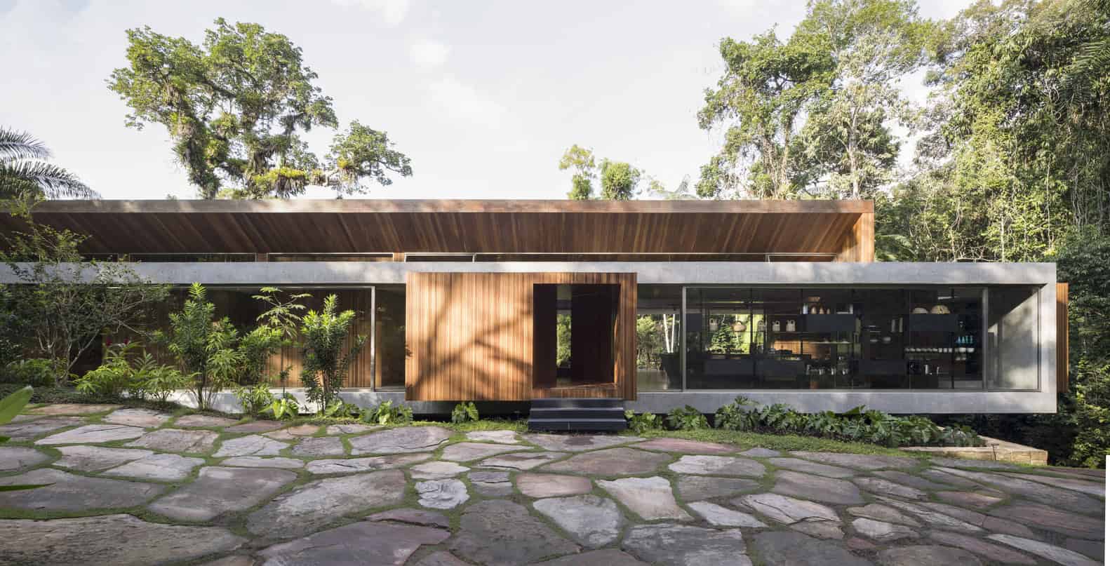 Contemporary modern house with sleek architectural design featuring wood and glass elements, surrounded by lush greenery and natural stone pathway.