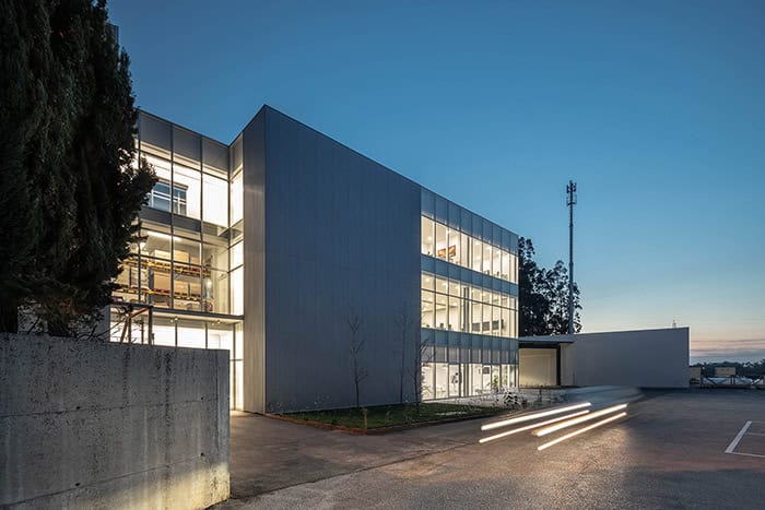 Modern minimalist commercial office building with large glass windows and sleek architectural design at dusk.