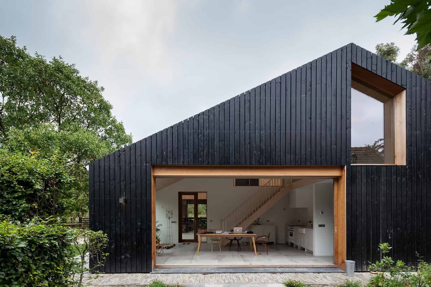 Contemporary black wooden house with large open indoor-outdoor living space and modern minimalist design, surrounded by greenery.