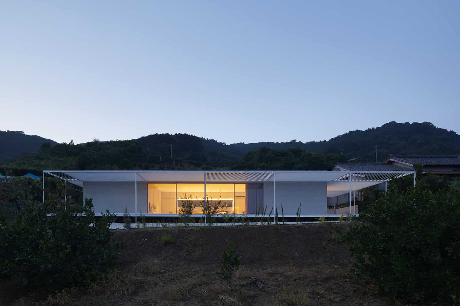 Modern minimalist house with sleek design and large glass windows at dusk under a mountain landscape.