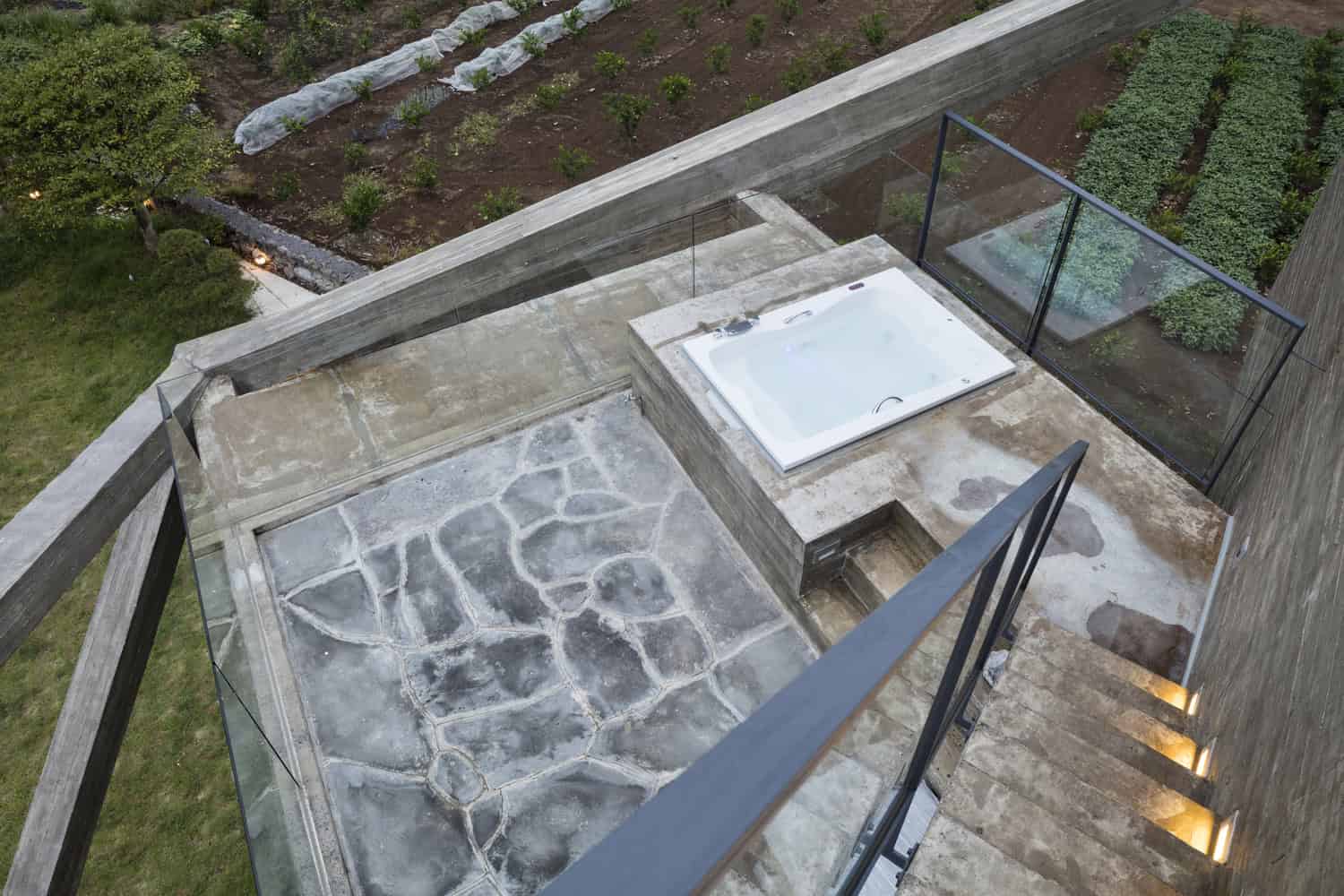1. Modern rooftop hot tub with glass railing overlooking a landscaped garden and stone patio in a contemporary home design.