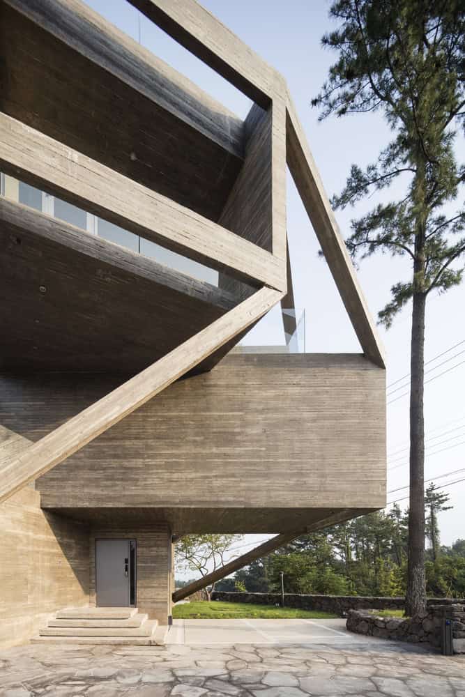 Industrial modern concrete architecture with bold geometric design and open-air elements, set against trees and a clear sky.