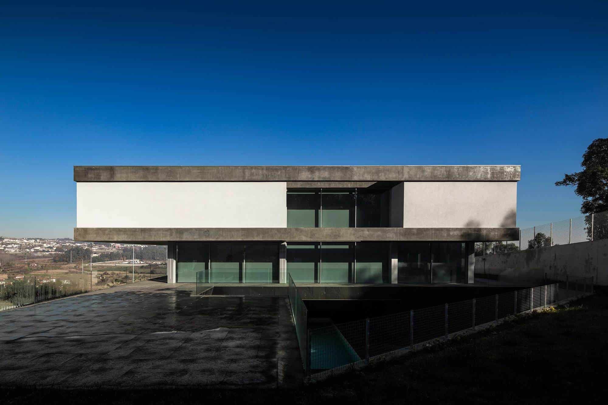 Sleek modern house with minimalist concrete accents, large glass windows, and an expansive outdoor patio under a clear blue sky. Innovative architecture blending contemporary design with natural surroundings.