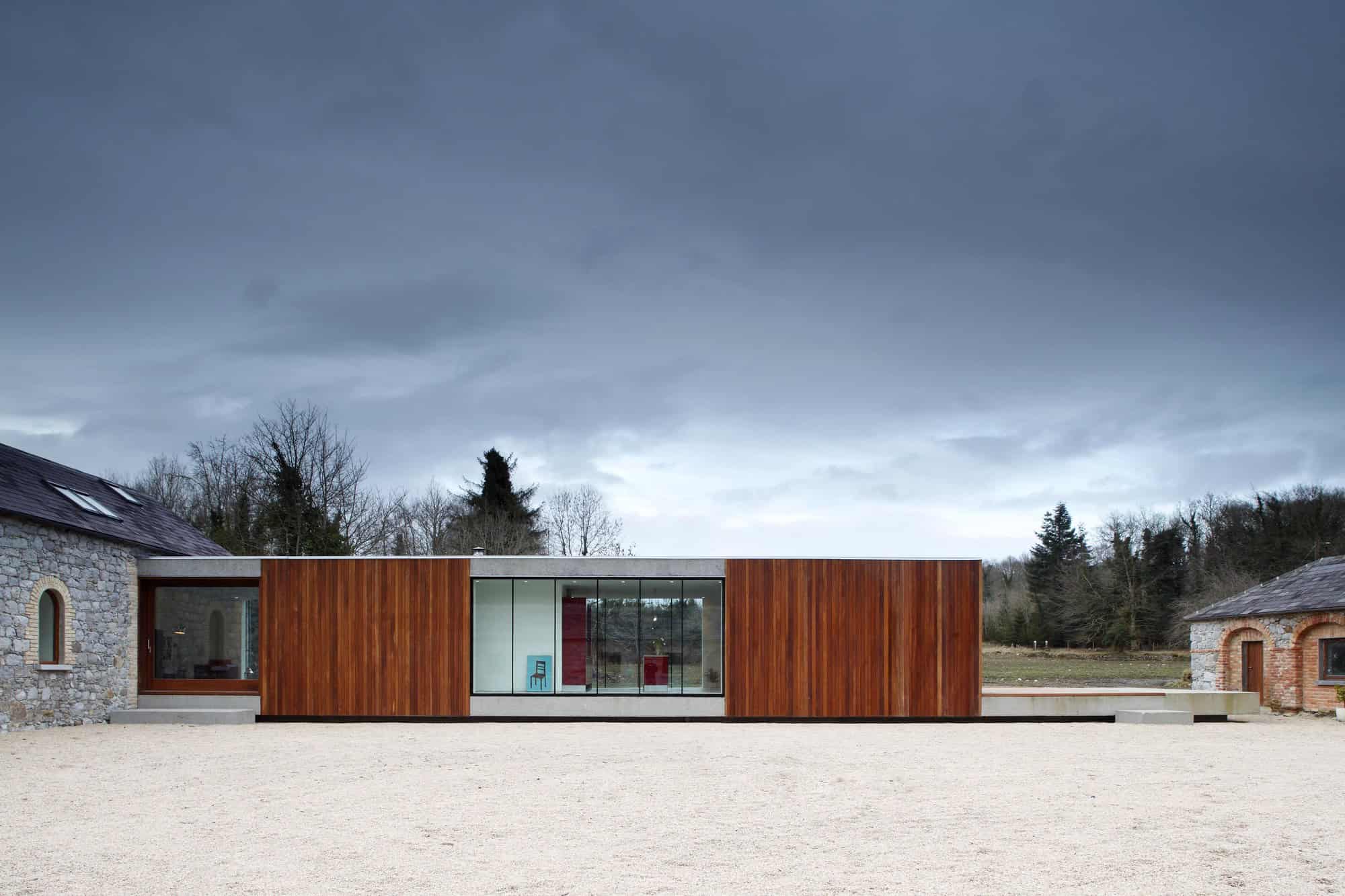 Sleek modern house with warm wooden exterior and large glass windows, blending contemporary architecture with rustic surroundings, under dramatic cloudy sky.